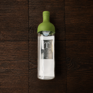 Hario Filter-in Bottle für Cold Brew Tee mit grünem Deckel auf dunklem Holztisch. Produkt aus dem iūgen Shop.