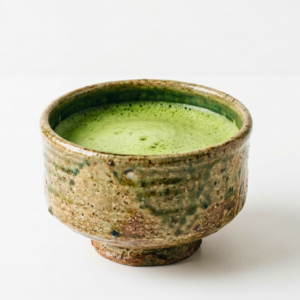 braune Matcha Schale mit schmalem Fuß, Matcha ist bis fast zum Rand der Schale eingefüllt.