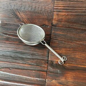 Feines Teesieb (Chakoshi) aus Edelstahl mit langem Griff auf dunklem Holztisch. Produkt aus dem iūgen Shop.