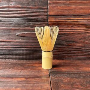 Japanischer Matcha-Besen aus goldenem Bambus (Chasen) auf dunklem Holztisch. Produkt aus dem iūgen Shop.