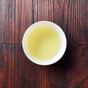 Tasse mit aufgebrühtem Genmaicha-Tee auf dunklem Holztisch aus der Draufsicht. Produkt aus dem iūgen Shop.