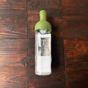 Hario Filter-in Bottle für Cold Brew Tee mit grünem Deckel auf dunklem Holztisch. Produkt aus dem iūgen Shop.