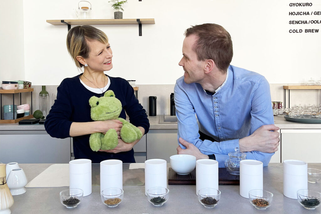 Dr. Christin Müller-Wenzel und Holger Müller stehen hinter einem Tisch mit verschiedenen Teesorten und Teezubehör und sprechen über iūgen –Matcha & Tea.