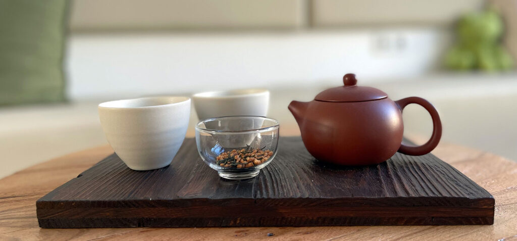 Teeset mit Teekanne, Tassen und Teeblättern auf einem dunklen Holztablett.