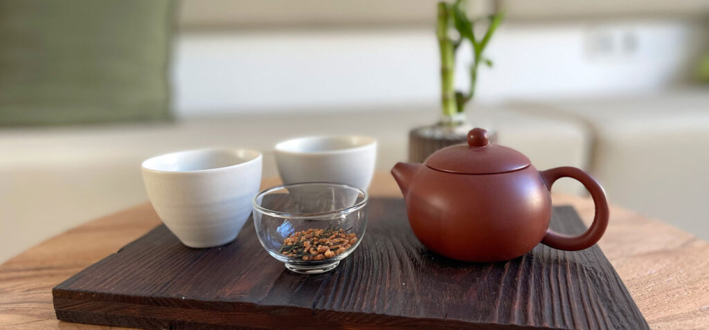 Teeset mit Teekanne, Tassen und Teeblättern auf einem dunklen Holztablett.