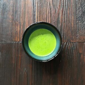 Schale mit frisch zubereitetem, hellgrünem Matcha-Tee auf dunklem Holztisch aus der Draufsicht.