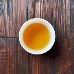 Tasse mit bernsteinfarbenem aufgebrühtem Oolong-Tee auf dunklem Holztisch aus der Draufsicht. Produkt aus dem iūgen Shop.