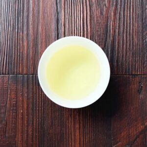 Tasse mit hellgrünem aufgebrühtem Sencha-Grüntee auf dunklem Holztisch aus der Draufsicht, Produkt aus dem iūgen Shop.