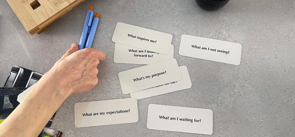 Hand hält Stifte über Karten mit Fragen zu Erwartungen, Inspiration und Zielen in einem Tee-Seminar für Unternehmen.