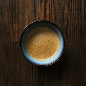 Schale mit frisch zubereitetem, leuchtend braunem Hojicha-Tee auf dunklem Holztisch aus der Draufsicht.