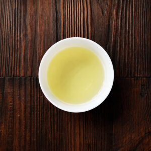 Tasse mit aufgebrühtem Genmaicha-Tee auf dunklem Holztisch aus der Draufsicht. Produkt aus dem iūgen Shop.