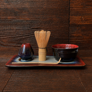 Matcha-Zubehör mit Chasen, Chashaku, Chasenhalter und Matcha-Schale auf dunklem Keramiktablett.