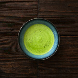 Schale mit frisch zubereitetem, leuchtend grünem Matcha-Tee auf dunklem Holztisch aus der Draufsicht.