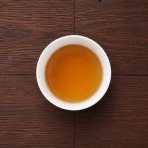 weiße Tasse mit aufgebrühtem Hoji-Genmaicha-Tee auf dunklem Holztisch aus der Draufsicht. Produkt aus dem iūgen Shop.